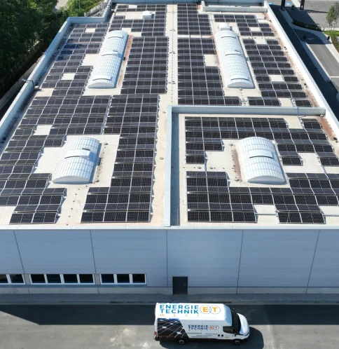 Solarpaneele bedecken Dach eines großen Gebäudes; Lieferwagen mit „Energie Technik“ davor geparkt.