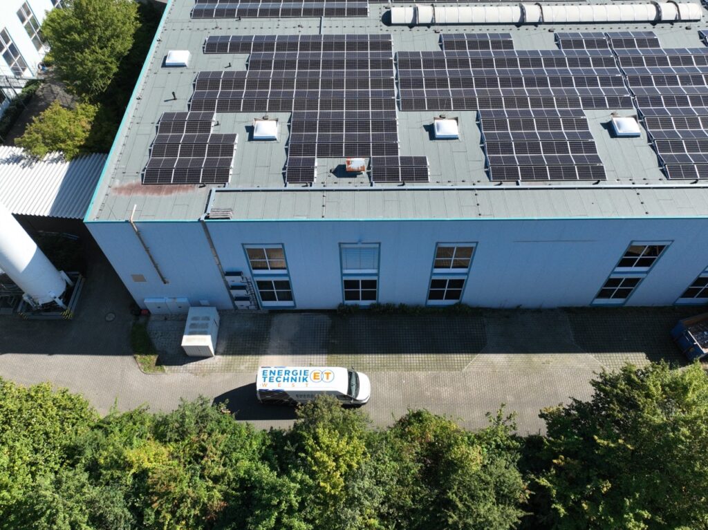 Solarpaneele bedecken Dach eines großen Gebäudes; Lieferwagen mit „Energie Technik“ davor geparkt.