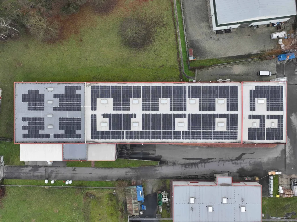 Solarmodule bedecken Dach eines großen Gebäudes, umgeben von Grünflächen und anderen Strukturen.