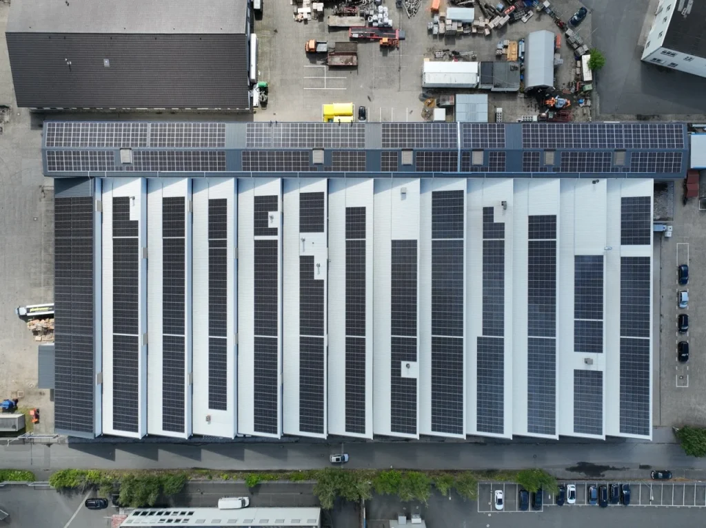Dach mit Solarmodulen, Installation, auf einem großen Industriegebäude, umgeben von Parkplatz und Straßen.