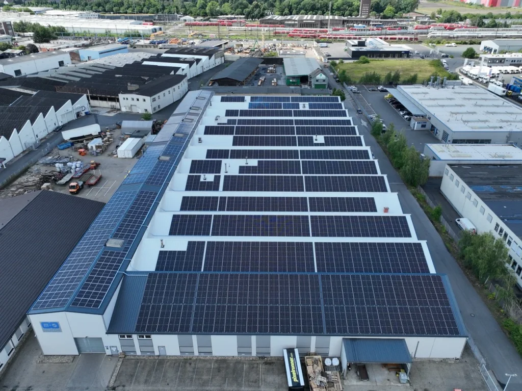 Solarmodule bedecken Flachdach eines großen Industriegebäudes in einer urbanen Gewerbegebietsumgebung.