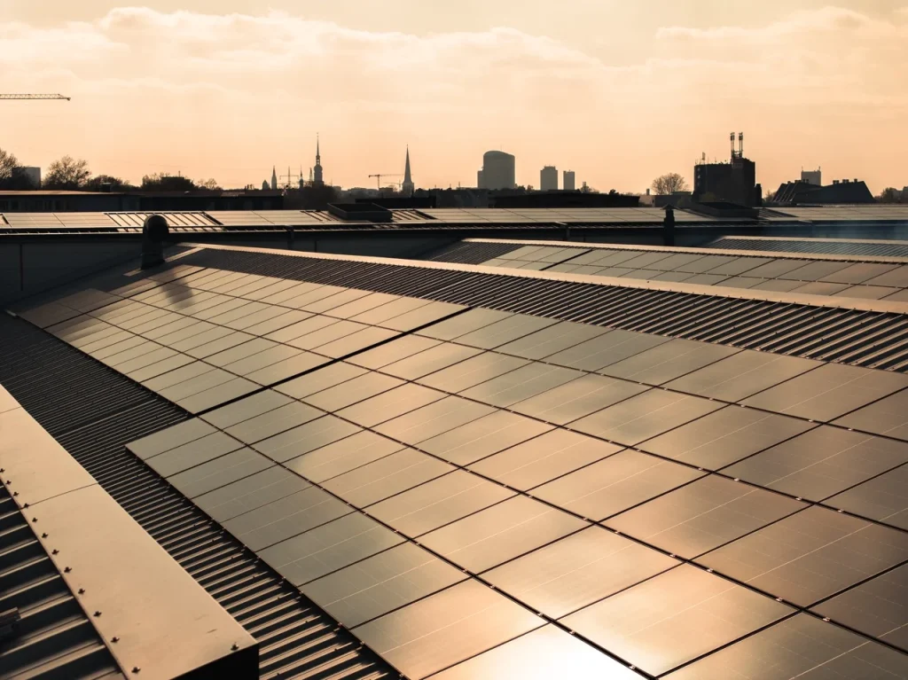 Solaranlagen reflektieren Sonnenlicht auf einem Dach vor städtischer Skyline im Abendlicht.