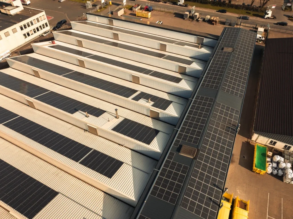 Solarmodule bedecken Fabrikdach, sammeln Sonnenenergie, umgeben von Industrieanlagen und Lastwagen im Hof.