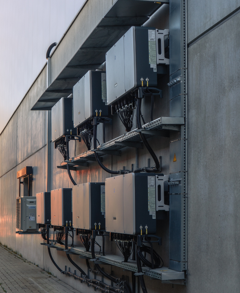 Elektrische Geräte hängen an Wand, verbunden mit Kabeln, in einem industriellen Außenbereich montiert.