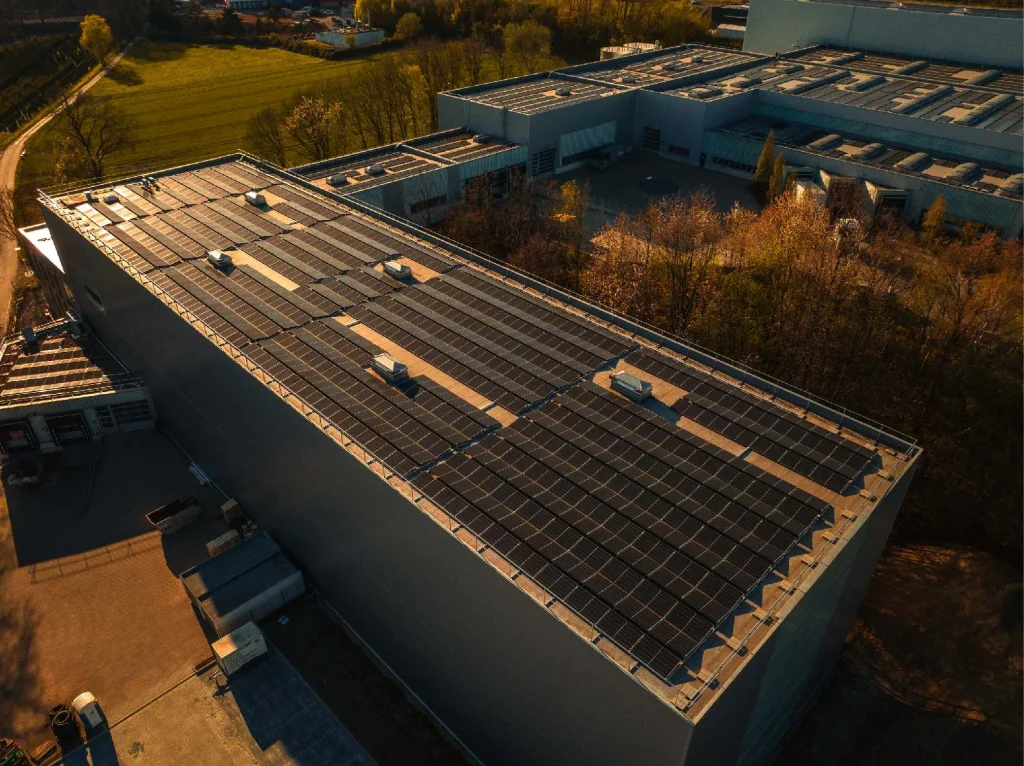 Solarpaneele bedecken das Dach eines großen Industriegebäudes neben blühenden Bäumen im Frühling.