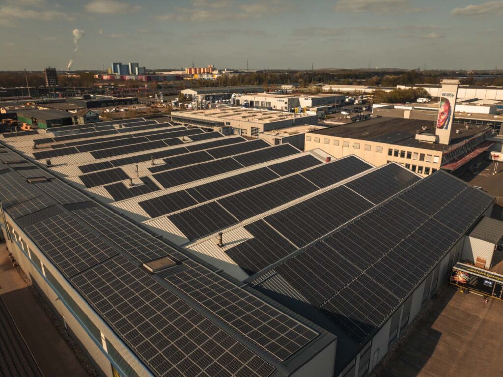 Solarzellen bedecken Dächer großer Gebäude in einem Industriegebiet unter blauem Himmel.