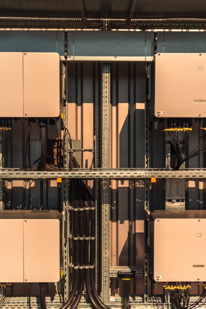 Elektrische Boxen befestigt an Metallrahmen, verbunden durch Kabel, in einem technischen Raum.