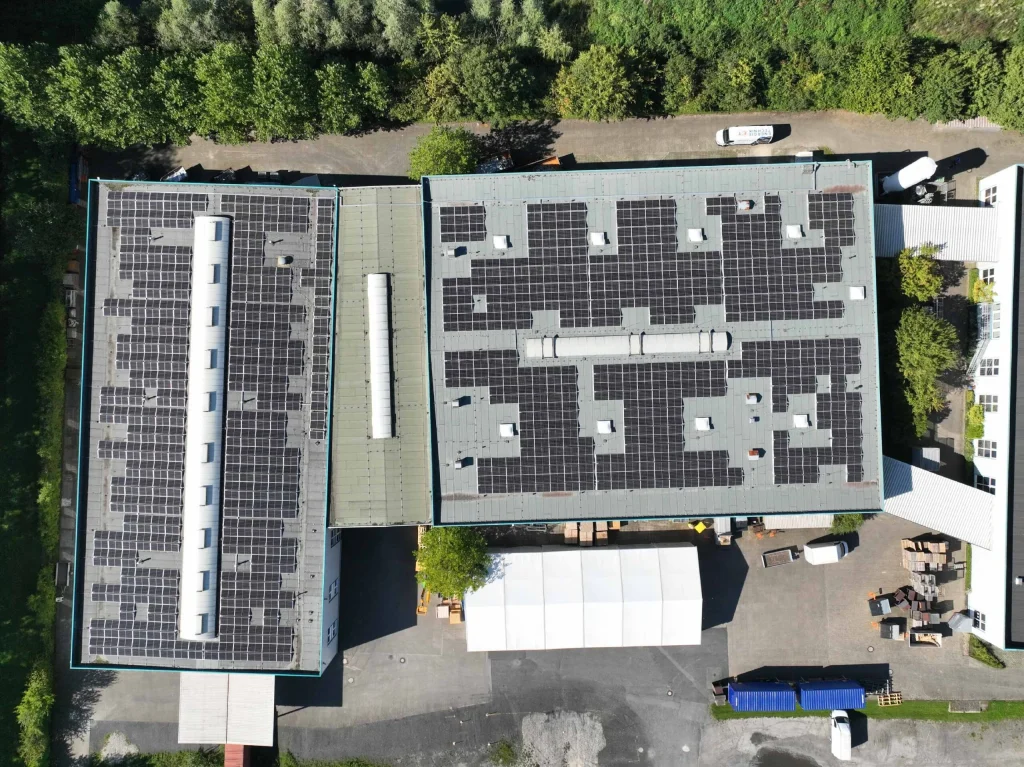 Dach mit Solarmodulen bedeckt, in einem Industriegebiet mit umliegenden Bäumen und Autos.