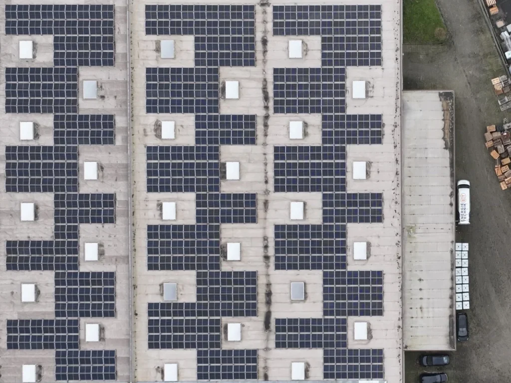 Solarmodule bedecken Dach eines großen Industriegebäudes; weiße Oberlichter verteilen sich regelmäßig.