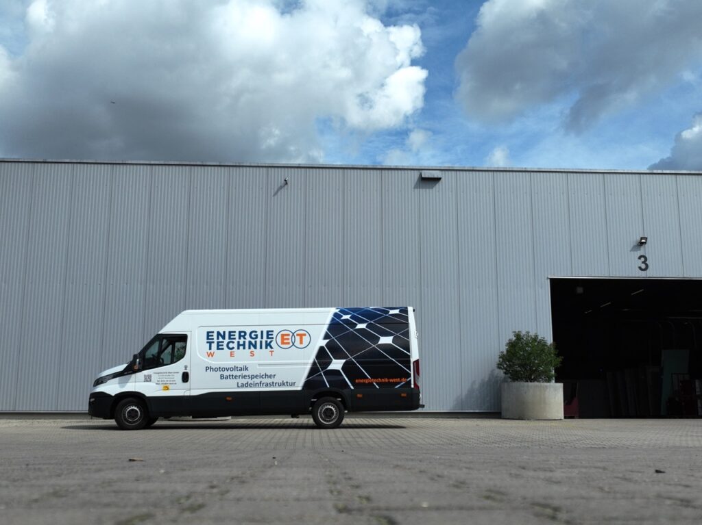 Lieferwagen steht vor einem grauen Gebäude mit Lagerhallen in einer Industrieumgebung.