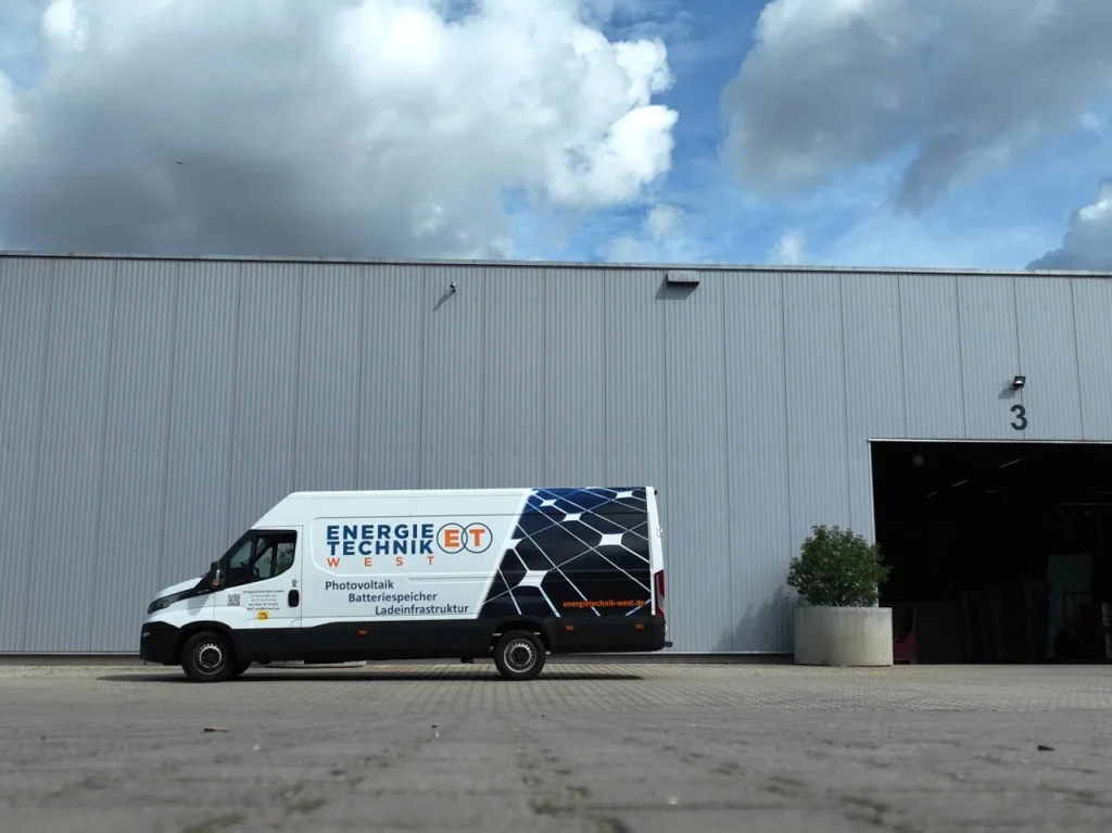 Lieferwagen steht vor einem grauen Gebäude mit Lagerhallen in einer Industrieumgebung.