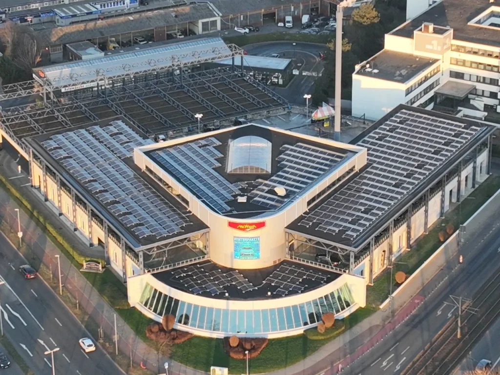 Gebäude mit Solarpanels steht in städtischer Umgebung, umgeben von Straßen und anderen Gebäuden.