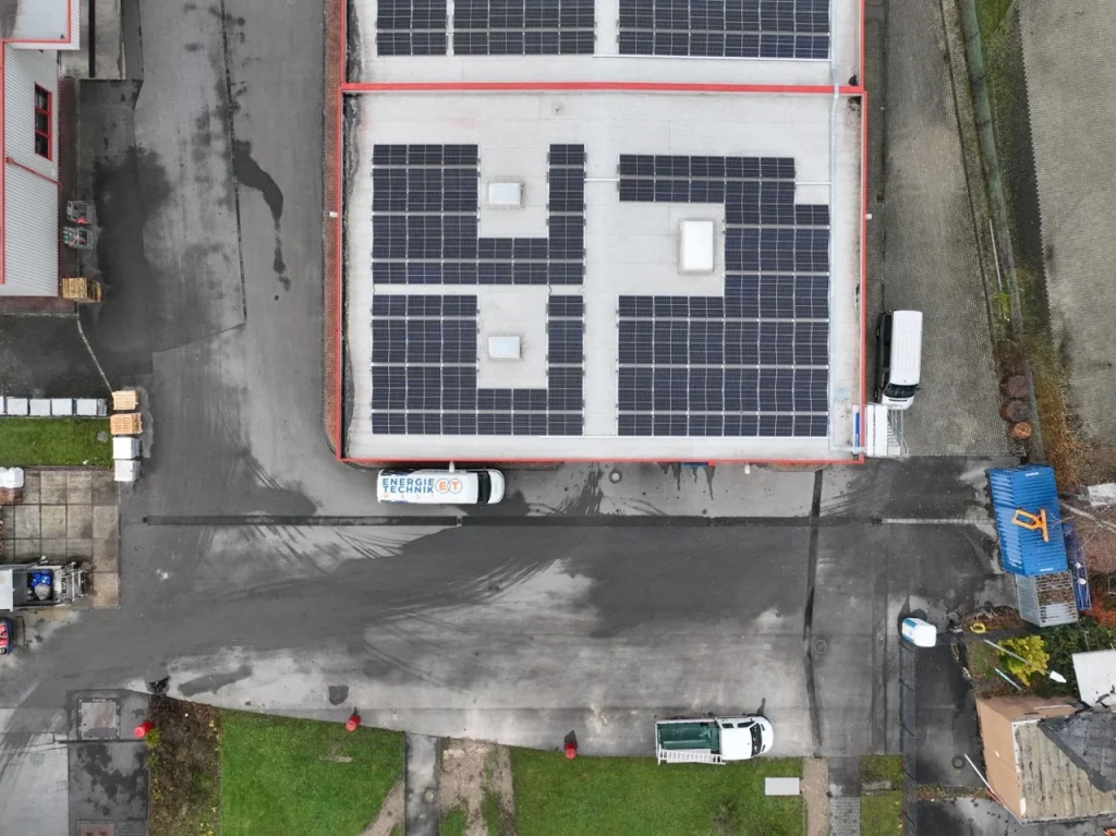 Dach mit Solarmodulen, neben geparkten Fahrzeugen, in einem Industriegebiet. Fahrzeugbeschriftung: "Energie-Technik".