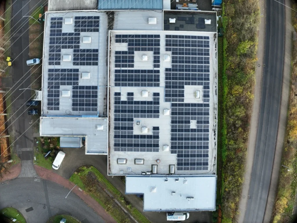 Dach mit Solarpanelen, von oben betrachtet, umgeben von Straßen und Vegetation.