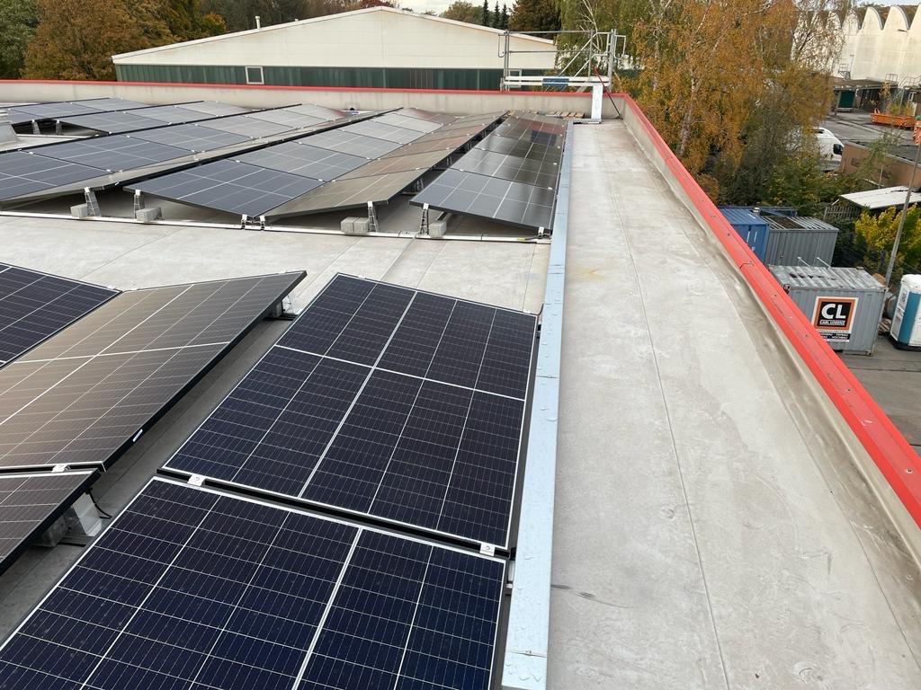 Solarmodule sind installiert, liegen flach auf einem Flachdach in einem industriellen Gebiet.