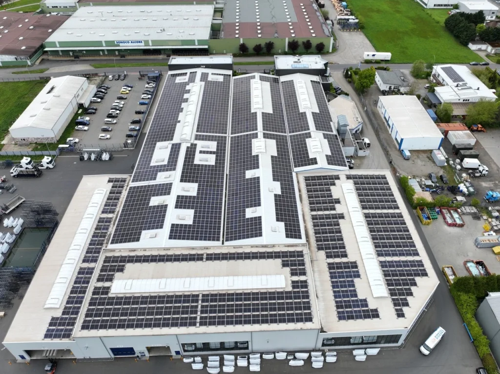 Dach, Sonnenkollektoren, Industriegebiet: Solarmodule bedecken großflächig Fabrikdach, umgeben von grünen Flächen.