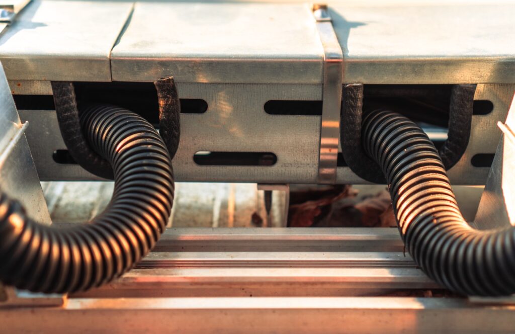Schwarze Kabel verlaufen durch Metallkanäle in industrieller Umgebung.