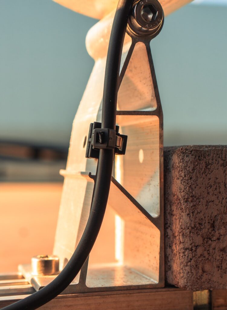 Kabel befestigt an Metallstrebe, neben Ziegelstein, in einer industriellen Umgebung.