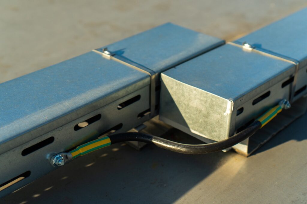 Metallkasten – enthält Kabel – auf grauer Oberfläche befestigt, mit gelb-grünen Markierungen an Kabeln.