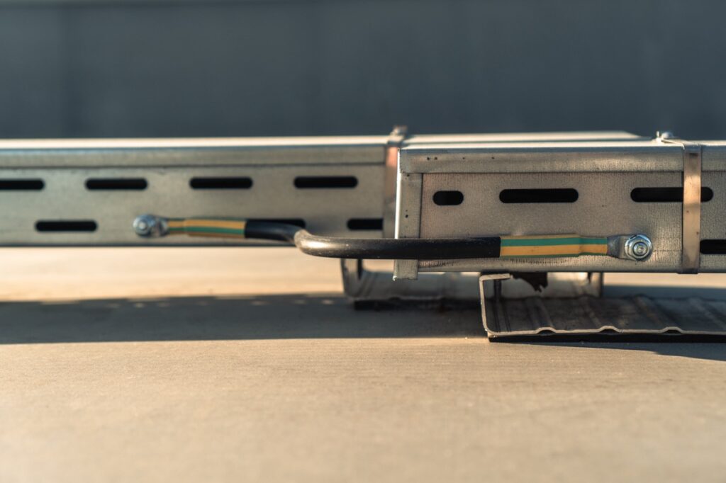 Metallkabelkanal mit Kabeln verläuft horizontal über grauem Boden, befestigt durch Schrauben.