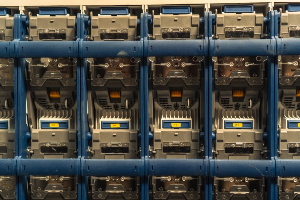 Schaltkästen stehen nebeneinander in einem technischen Raum, mit Kabeln und blauen Rahmen.