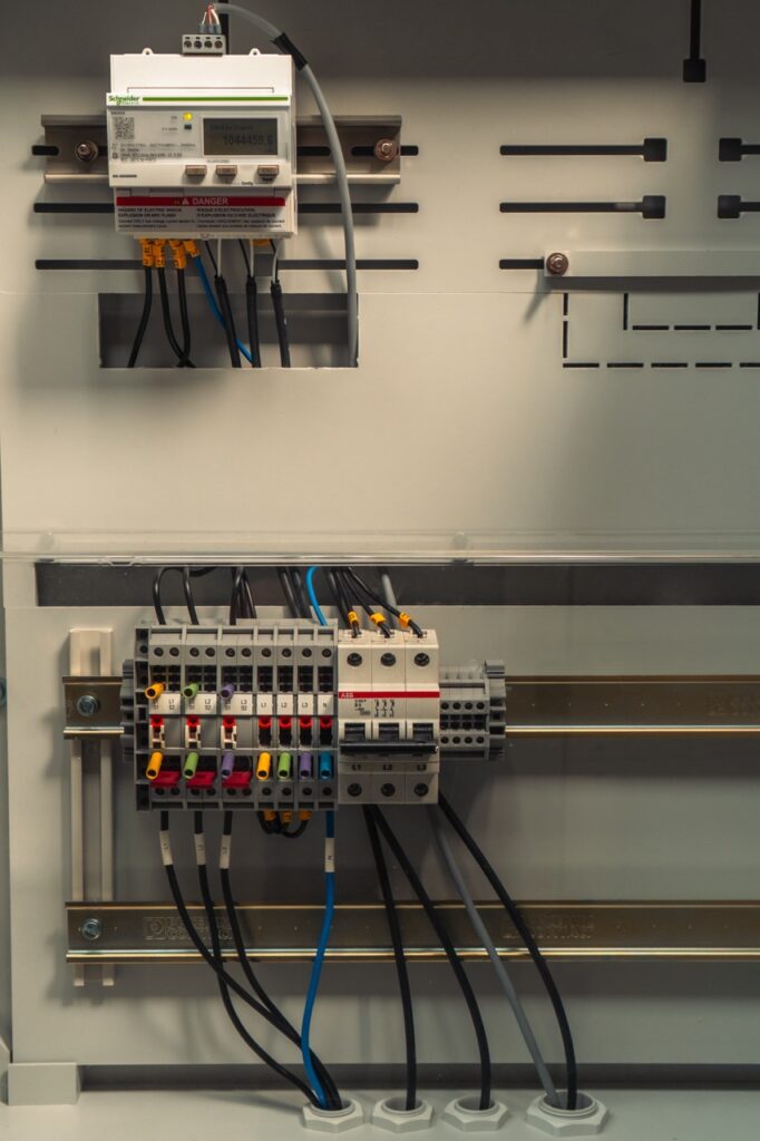 Stromzähler und Schalttafelleiste verbinden Kabel in einem grauen Schaltschrank.