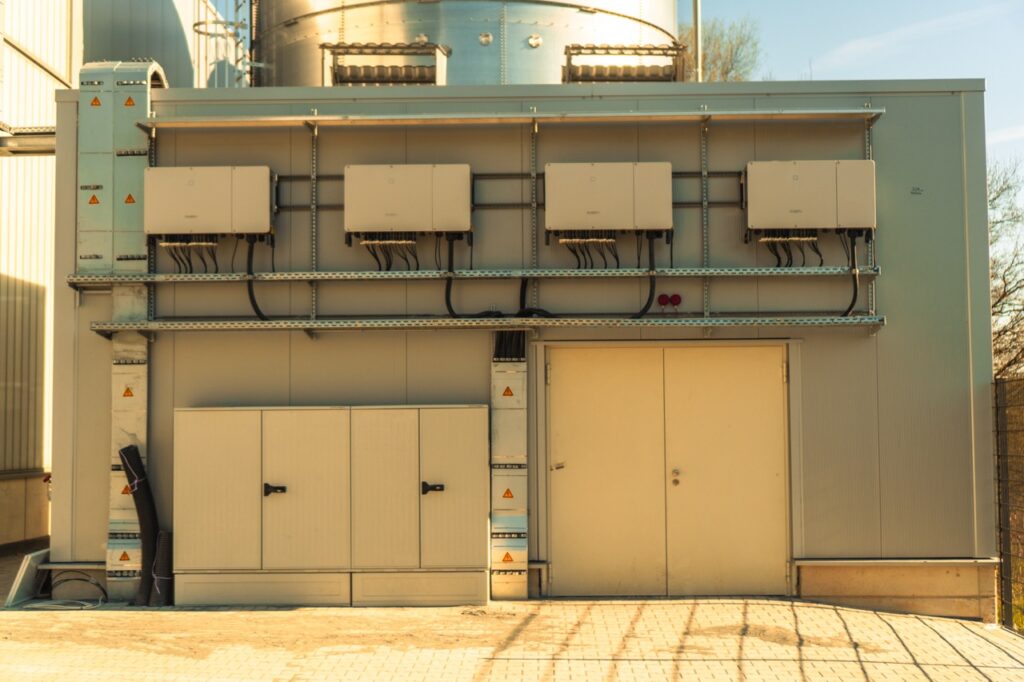 Grau gestrichener Industrie-Metallschuppen; Lüftungssysteme montiert; sonniger Außenbereich mit gepflastertem Boden.