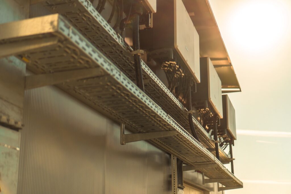 Metallstruktur hält Geräte mit Kabeln, montiert an einer Wand, mit Sonnenlicht im Hintergrund.