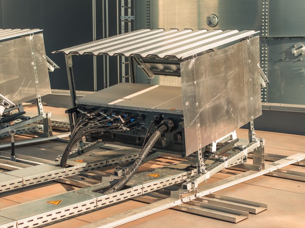 Elektronikkasten mit Kabeln, geschützt durch Metallabdeckung, auf Industrieboden montiert.