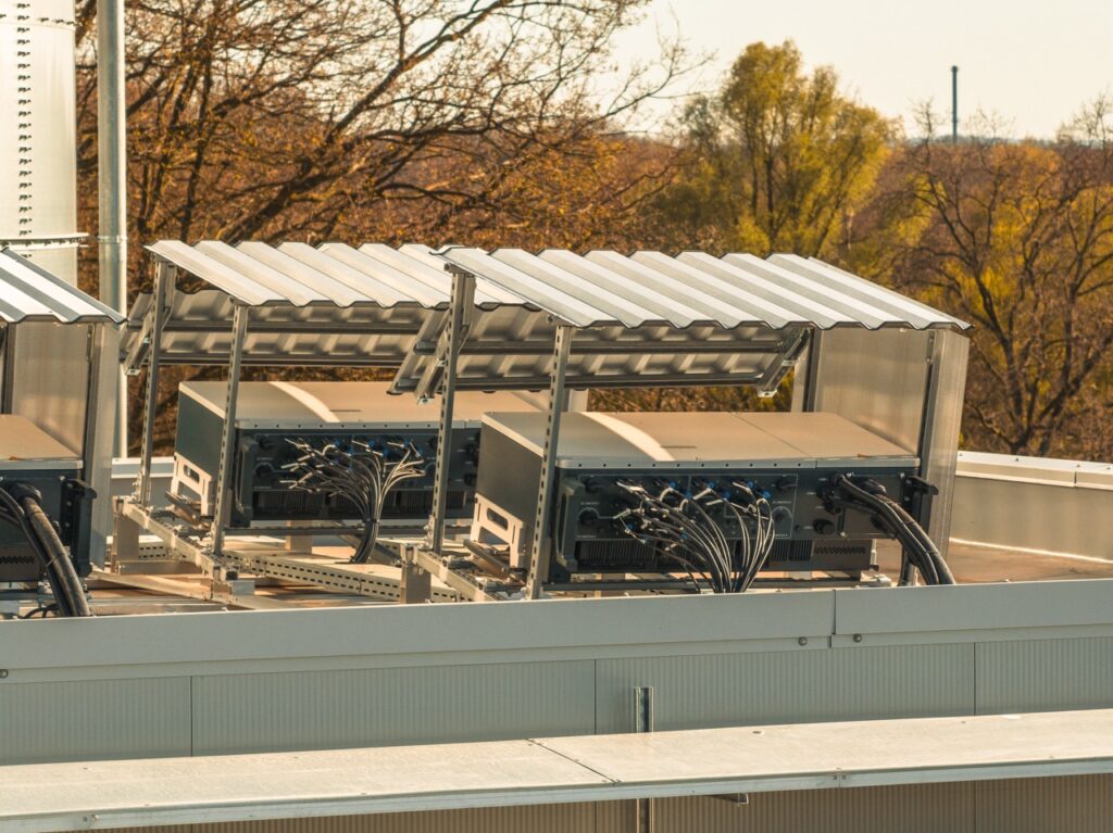 Metallgeräte auf einem Dach, verbunden durch Kabel, in einer bewaldeten Umgebung.