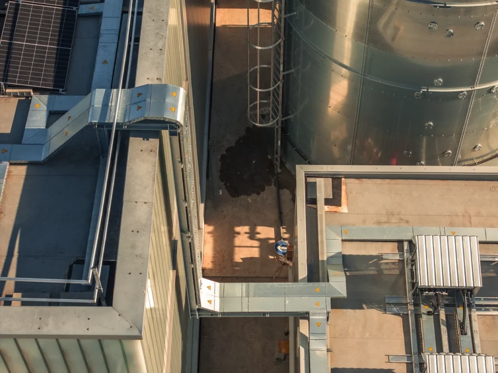 Industrieanlagen wirken statisch, großes Rohr- und Tanksystem, Sonnenlicht erzeugt Schatten auf Betonfläche.