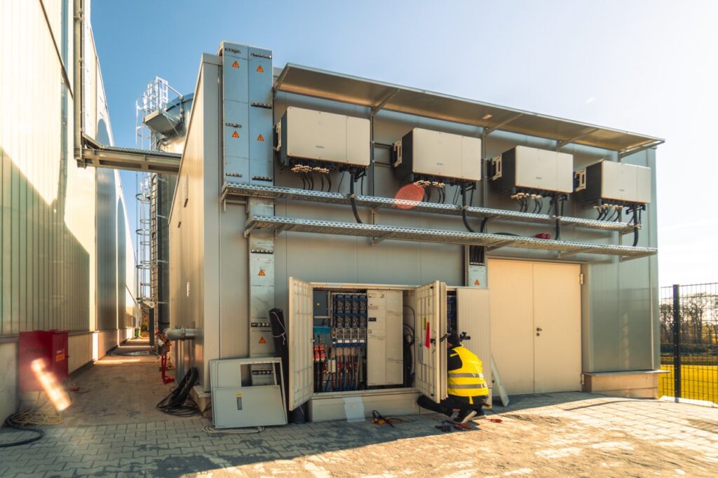 Ein Techniker wartet einen offenen Schaltschrank neben einem großen Gebäude im Freien.