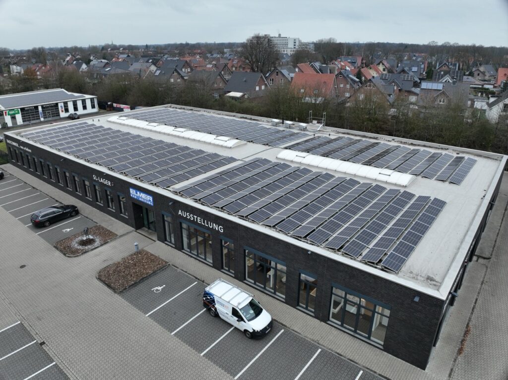 Solarmodule bedecken das Dach eines Gebäudes mit Ausstellungsraum, umgeben von geparkten Autos.