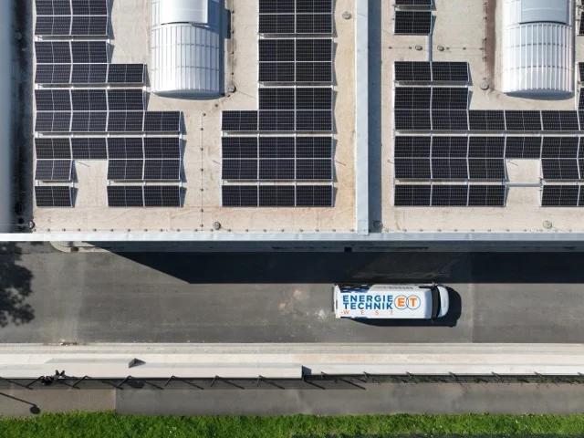 Transporter fährt neben Gebäude mit Sonnenkollektoren auf dem Dach.