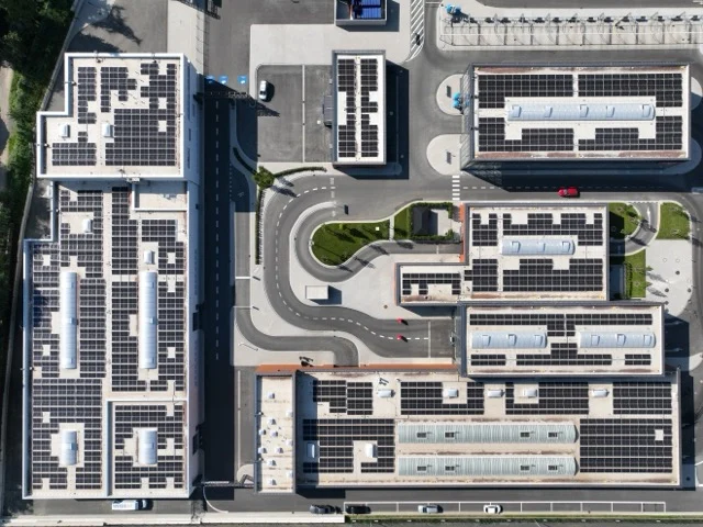 Solarmodule bedecken Gebäude, die von Straßen umgeben sind; Vogelperspektive auf einem sonnigen Tag.