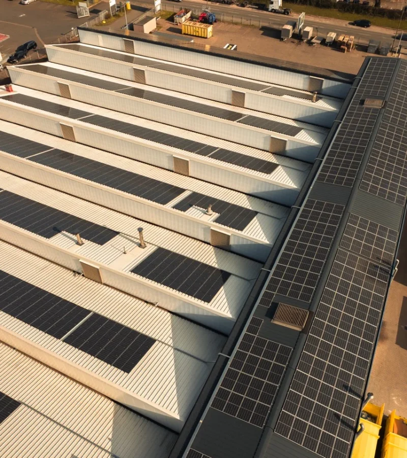 Solarmodule bedecken Fabrikdach, sammeln Sonnenenergie, umgeben von Industrieanlagen und Lastwagen im Hof.